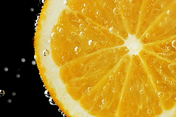 Slice of orange in the water with bubbles, on black background — Stock Photo, Image