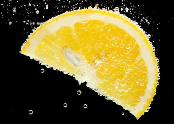 Fatia de laranja na água com bolhas, no fundo preto — Fotografia de Stock
