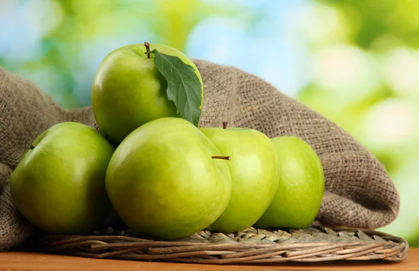 Ripe green apples with leaves on burlap, on wooden table, on green backgrou — Stock Photo, Image