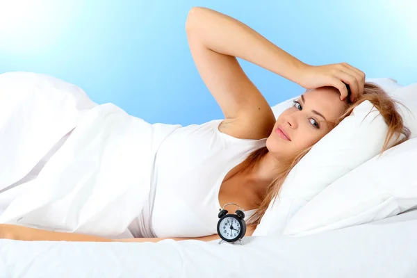 Jeune belle femme couchée sur le lit avec réveil sur fond bleu — Photo