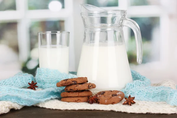 Brocca e bicchiere di latte con biscotti su girocollo maglieria su tavola di legno — Foto Stock