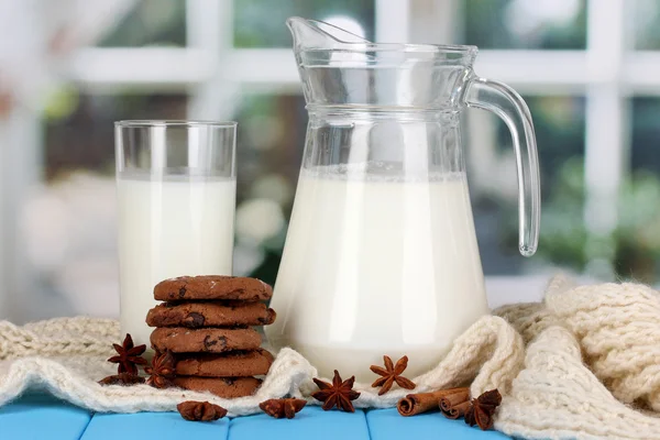 Brocca e bicchiere di latte con biscotti su girocollo maglieria su tavola di legno — Foto Stock