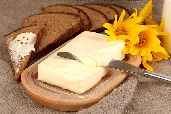 Масло на деревянном держателе в окружении хлеба и цветов на мешочке backgrou — стоковое фото