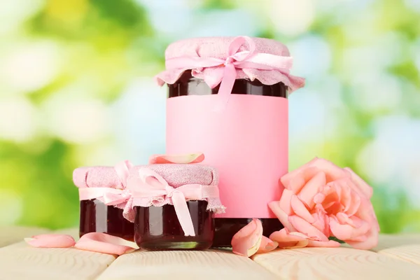 Frascos con mermelada de rosa y flor sobre mesa de madera sobre fondo verde —  Fotos de Stock