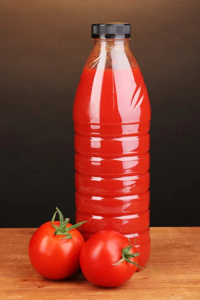 Tomato juice in bottle on wooden table on brown background — Stock Photo, Image