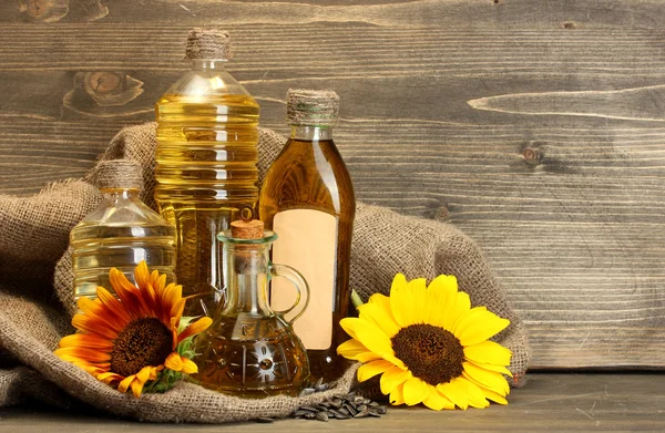 Olio in bottiglie, girasoli e semi, su fondo di legno — Foto Stock