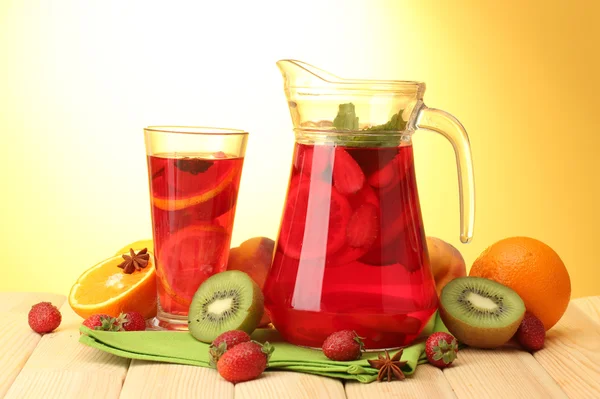 Sangria in Glas und Glas mit Früchten, auf Holztisch, auf gelbem Hintergrund — Stockfoto