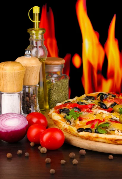 Delicious pizza with spices on wooden table on fire background — Stock Photo, Image