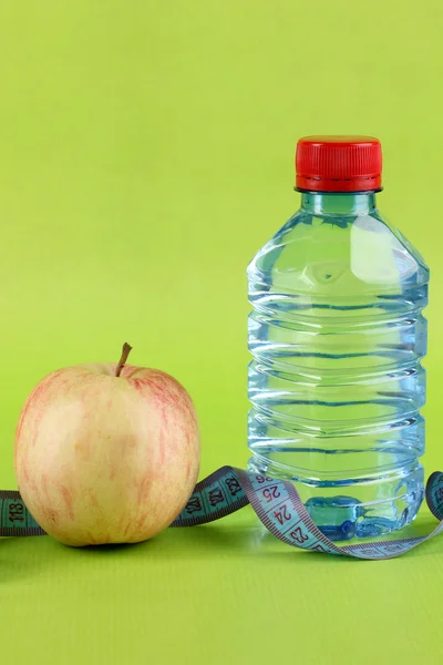 Botella de agua, manzana y cinta métrica sobre fondo verde — Foto de Stock