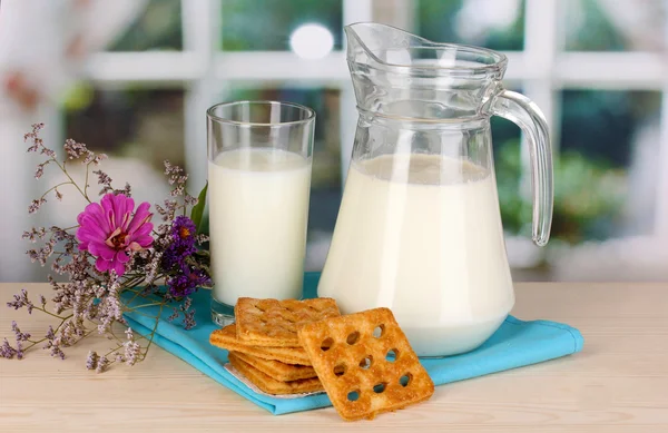 Kancsó és pohár tejet a cookie-kat a fából készült asztal, ablak háttér — Stock Fotó