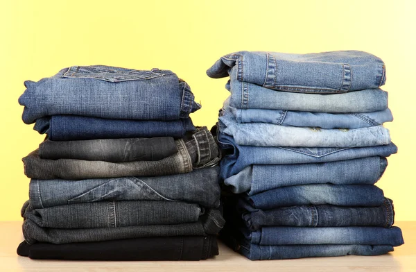 Många jeans staplade i en högar på gul bakgrund — Stockfoto