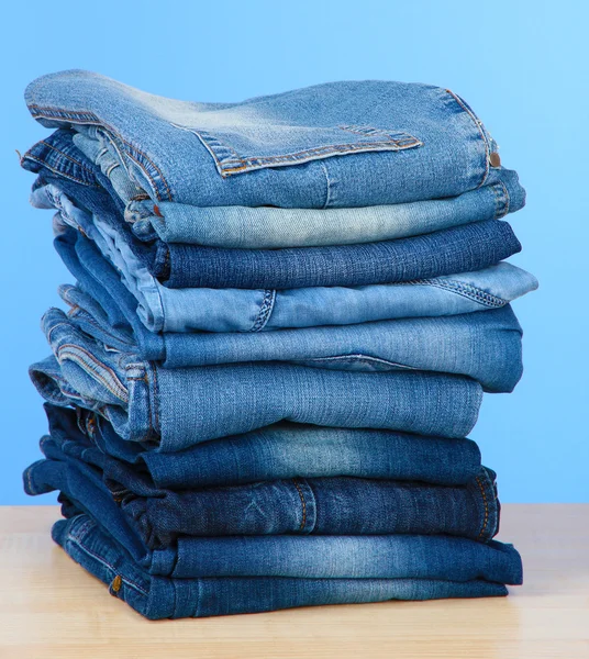 Beaucoup de jeans empilés dans une pile sur fond bleu — Photo