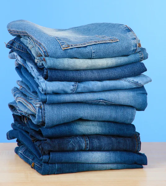 Many jeans stacked in a pile on blue background — Stock Photo, Image