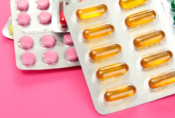 Capsules and pills packed in blisters, on pink background — Stock Photo, Image