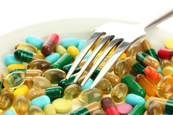 Красочные капсулы и таблетки на тарелке с вилкой, изолированные на белом — стоковое фото