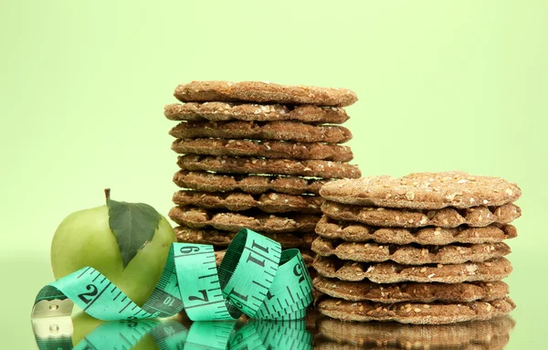 Tasty crispbread, apple and measuring tape, on green background — Stock Photo, Image