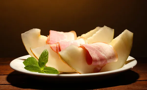 Parma ham and melon, on wooden table, on brown background — Stock Photo, Image