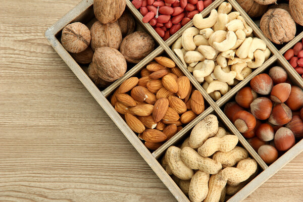 ассортимент вкусных орехов в деревянной коробке на столе
