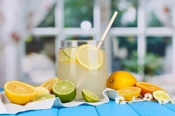Citrus lemonade in glass bank of citrus around on blue wooden table on wind — Stock Photo, Image