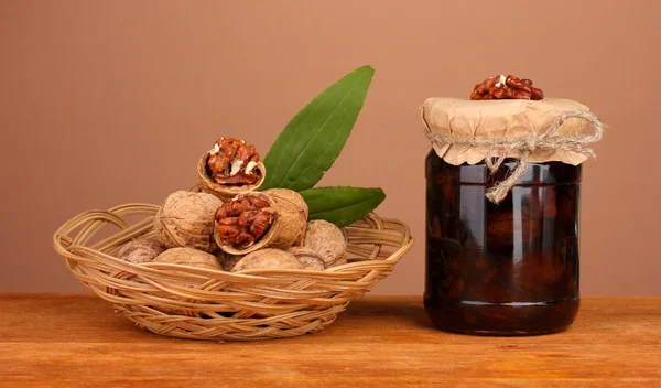 Jam-jar van walnoten op houten tafel en een mand met walnoten op bruine backg — Stockfoto