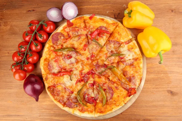 Tasty pepperoni pizza with vegetables on wooden board on wooden background — Stock Photo, Image