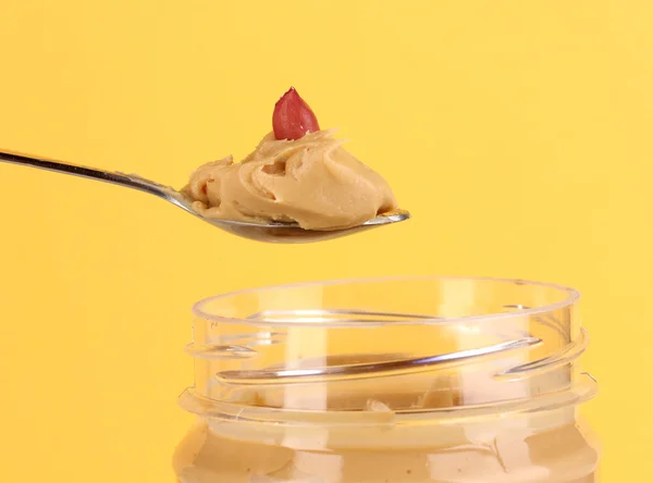 おいしいピーナッツ バターの瓶と黄色の背景にスプーンで — ストック写真