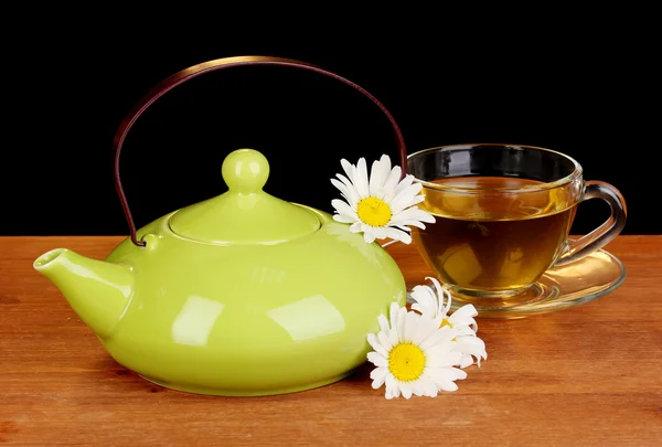 Чайник и чашка с ромашковым чаем на деревянном столе на коричневом фоне — стоковое фото