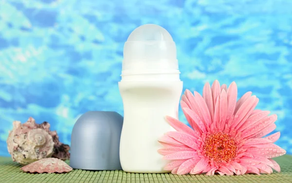 Дезодорант, цветок и раковины на синем фоне моря — стоковое фото