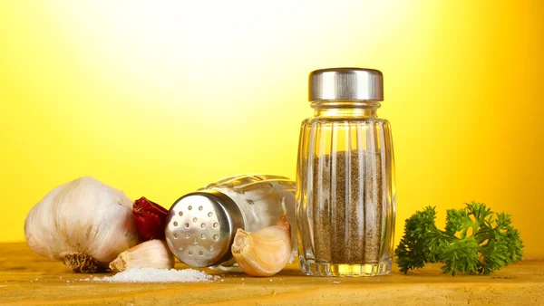 Αλάτι και ελαιοτριβεία πιπέρι, σκόρδο και μαϊντανό στο ξύλινο τραπέζι στο κίτρινο backgro — Φωτογραφία Αρχείου