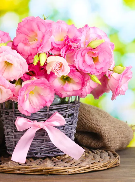 Букет цветов эустомы в плетеной вазе, на деревянном столе, на зеленой спинке — стоковое фото