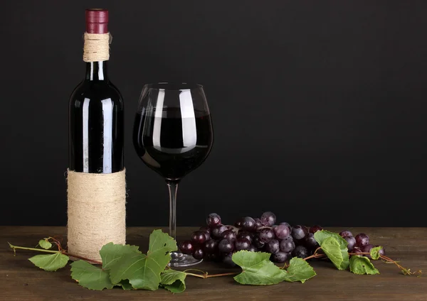 Μπουκάλι κρασί με το σταφύλι φύλλα στο ξύλινο τραπέζι σε μαύρο φόντο — Φωτογραφία Αρχείου