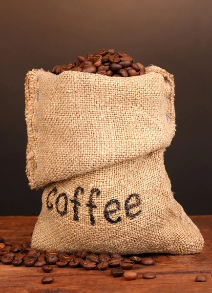 Grains de café en sac sur la table sur fond sombre — Photo