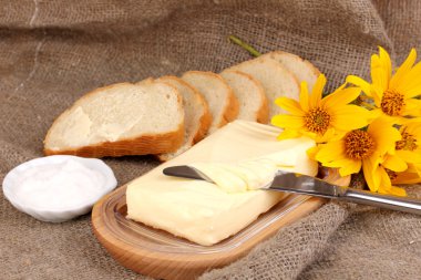 Ahşap kutusunda ekmek ve backgrou çuval bezi üzerinde çiçekler çevrili tereyağı