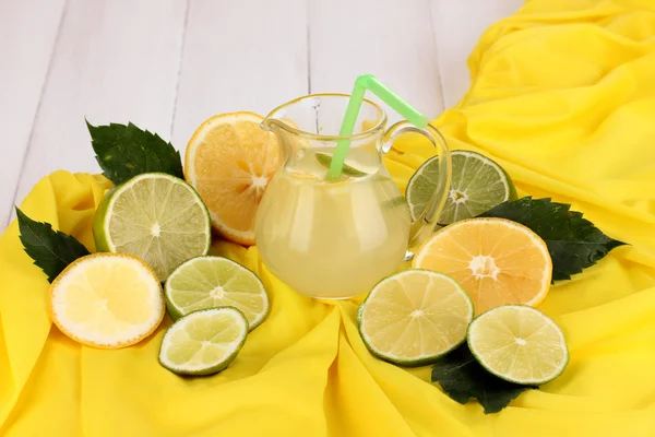 Limonada cítrica en jarra de cristal de cítricos alrededor en tela amarilla sobre blanco — Foto de Stock