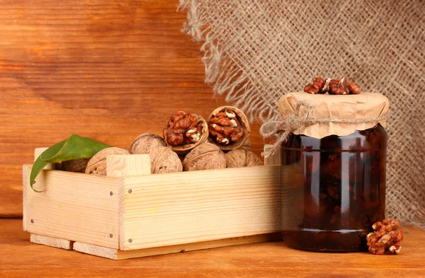 Jam-jar of walnuts and wooden box on wooden background — Stock Photo, Image