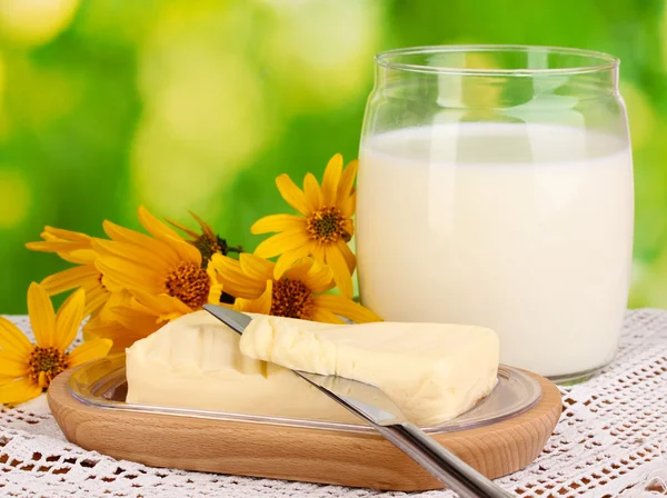 Mantequilla sobre soporte de madera rodeado de flores y leche sobre fondo natural —  Fotos de Stock