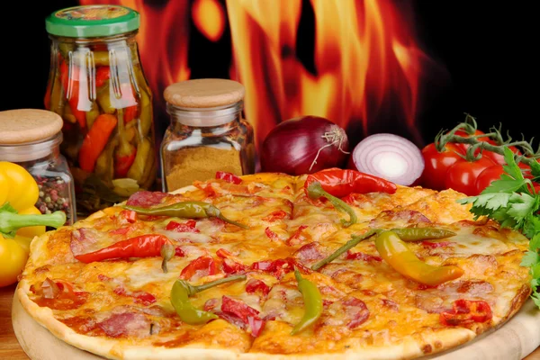 Tasty pepperoni pizza with vegetables on wooden board on flame background — Stock Photo, Image