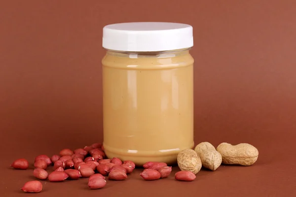 Delizioso burro di arachidi in vaso di arachidi vicino su sfondo marrone — Foto Stock