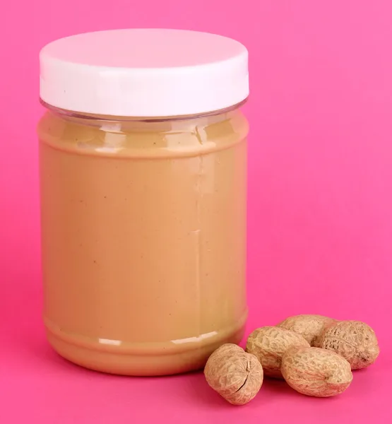 Delicious peanut butter in jar of peanut near on pink background — Stock Photo, Image