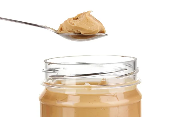 Смачне арахісове масло в банці і ложці ізольовано на білому — стокове фото