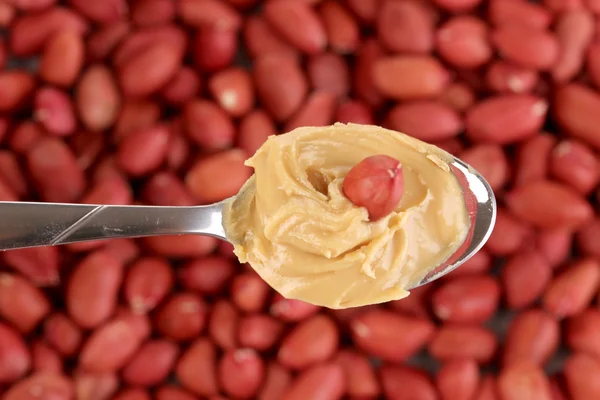 Delicious peanut butter in spoon on peanuts background close-up — Stock Photo, Image