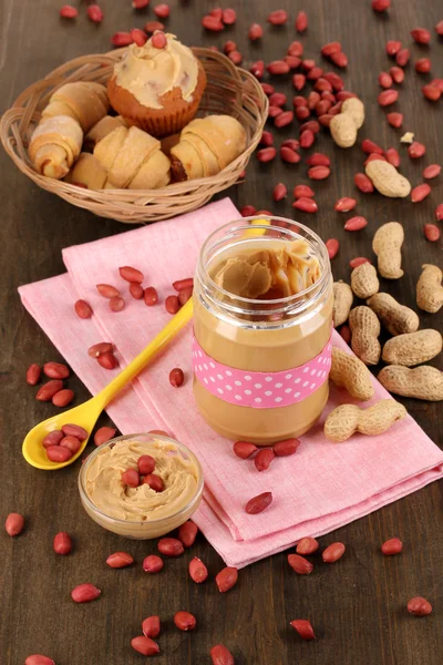 Deliciosa manteiga de amendoim em jarra com cozimento em guardanapo em mesa de madeira perto - — Fotografia de Stock