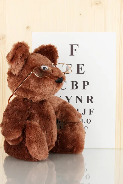 Teddy bear with glasses on eyesight test chart background close-up — Stock Photo, Image
