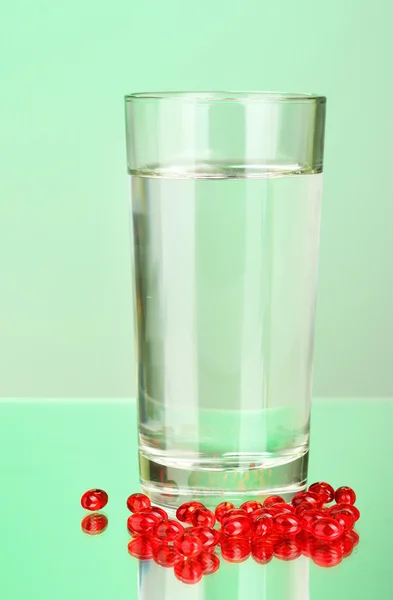 A glass of water and pills on green background close-up — Stock Photo, Image