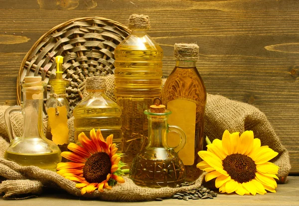 Oil in bottles, sunflowers and seeds, on wooden background — Stock Photo, Image