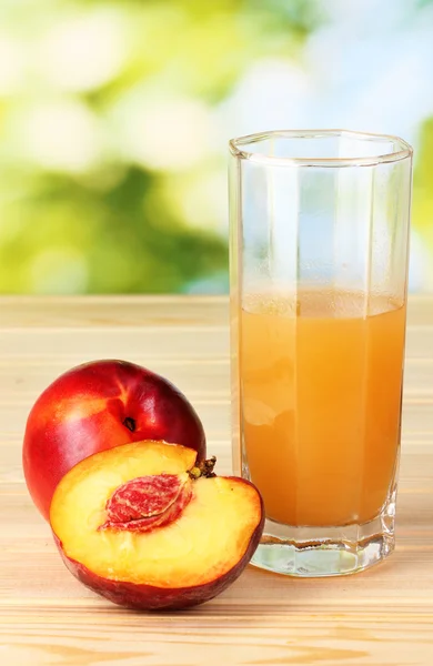 Ripe peaches and juice on wooden table on natural background — Stock Photo, Image