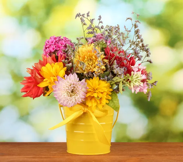 Balde amarelo brilhante com flores no fundo verde — Fotografia de Stock