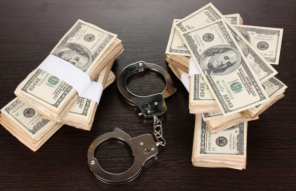 Handcuffs and packs of dollars on wooden table close-up — Stock Photo, Image