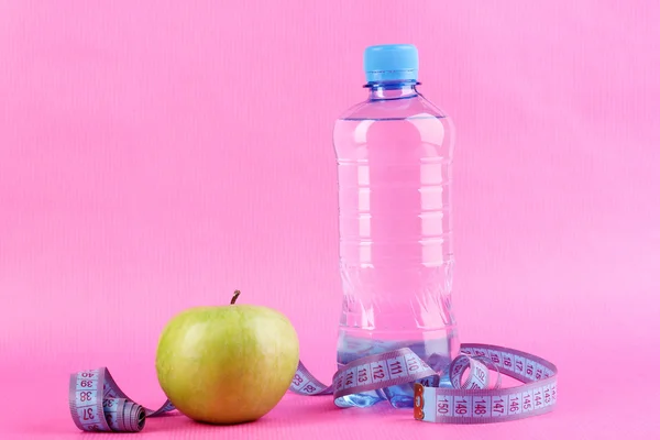 Şişe su, elma ve pembe bir arka plan üzerinde ölçüm bandı — Stok fotoğraf