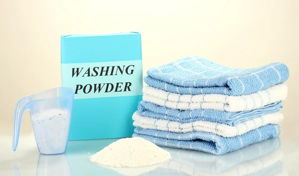 Box of washing powder with blue measuring cup and towels, isolated on white — Stock Photo, Image